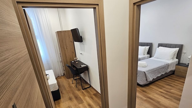 A hotel room with a wooden floor, a desk with a chair, a bed with two pillows, and a mounted TV. - B&B Lunis (Trieste)