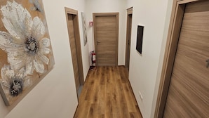 A hallway with wooden flooring, a large floral painting on the left, and wooden doors on both sides. - B&B Lunis (Trieste)