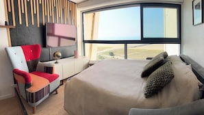 A modern hotel room with a large bed, a red and grey chair, a small desk, and a TV on the wall.