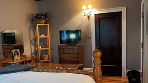 Une chambre à coucher avec un grand lit, une commode en bois, une télévision et une porte donnant sur une autre pièce.