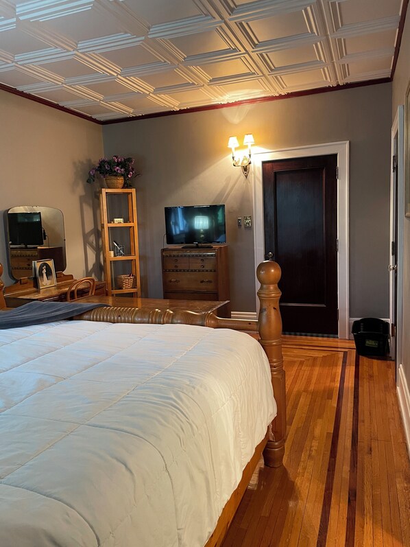 A bedroom with a large bed, wooden dresser, television, and a door leading to another room.