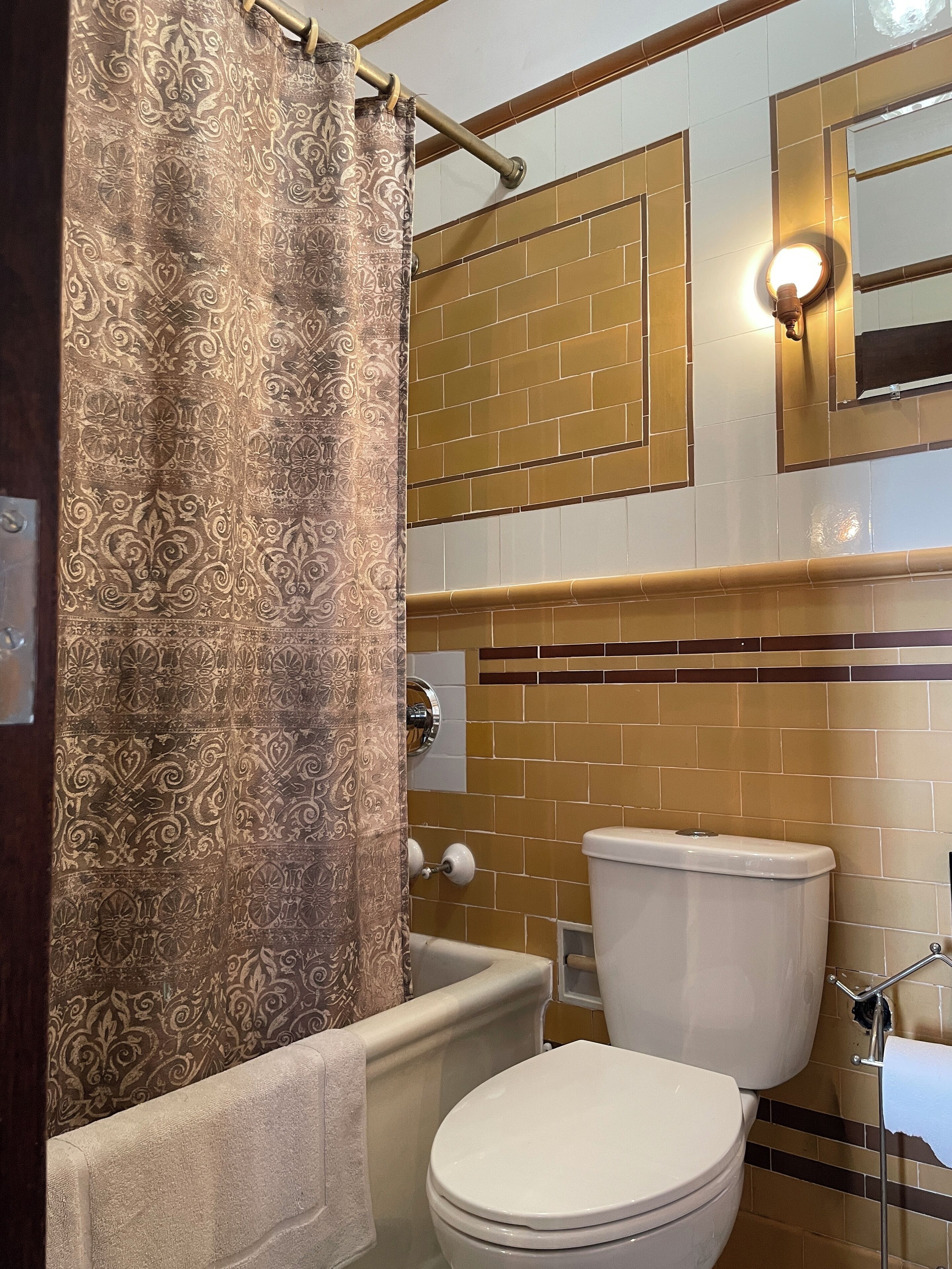 A bathroom with a patterned shower curtain, a white toilet, and a wall with a brick pattern.