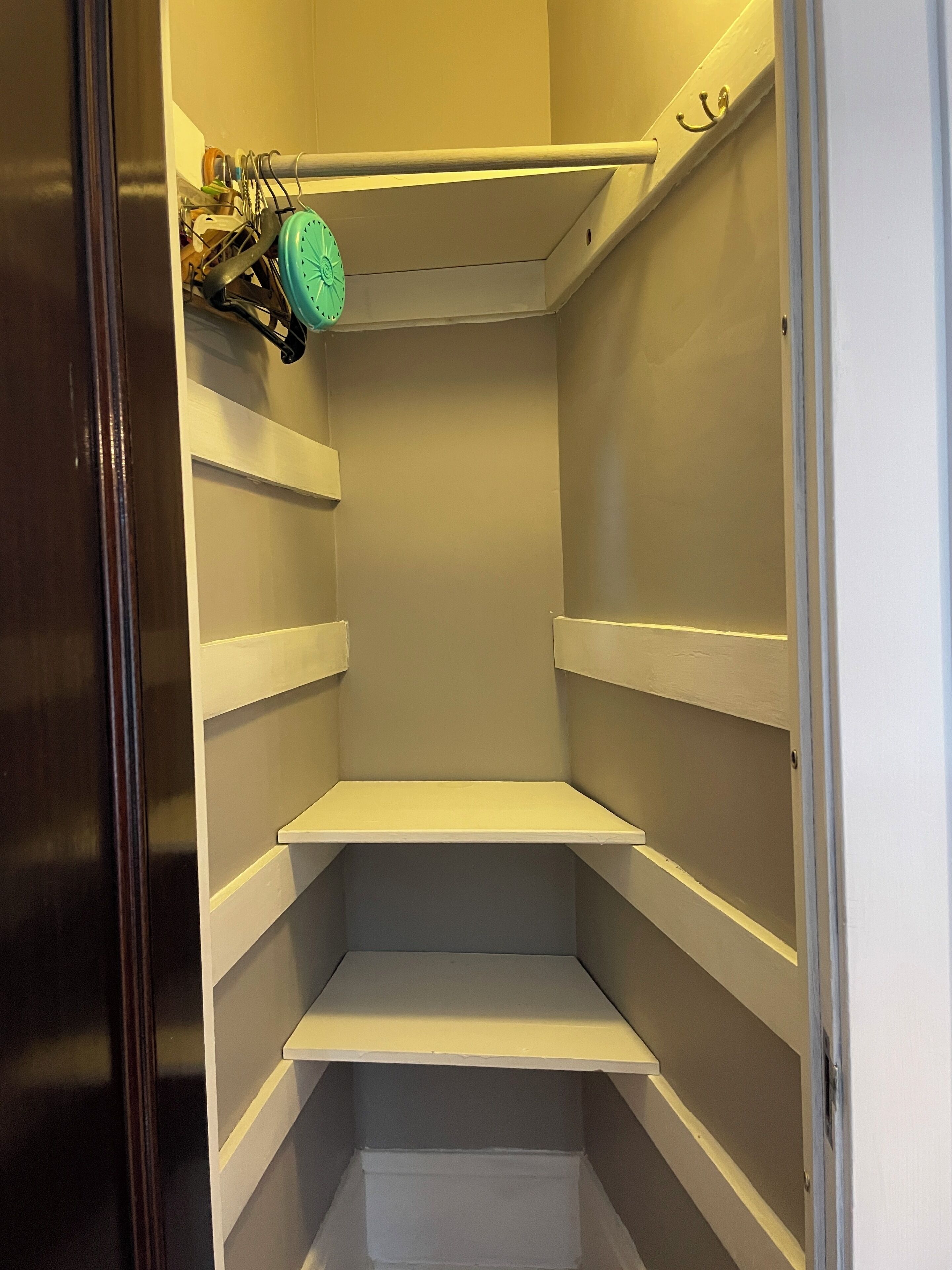 A small, empty walk-in closet with white shelves and a green towel hanging on a rack.