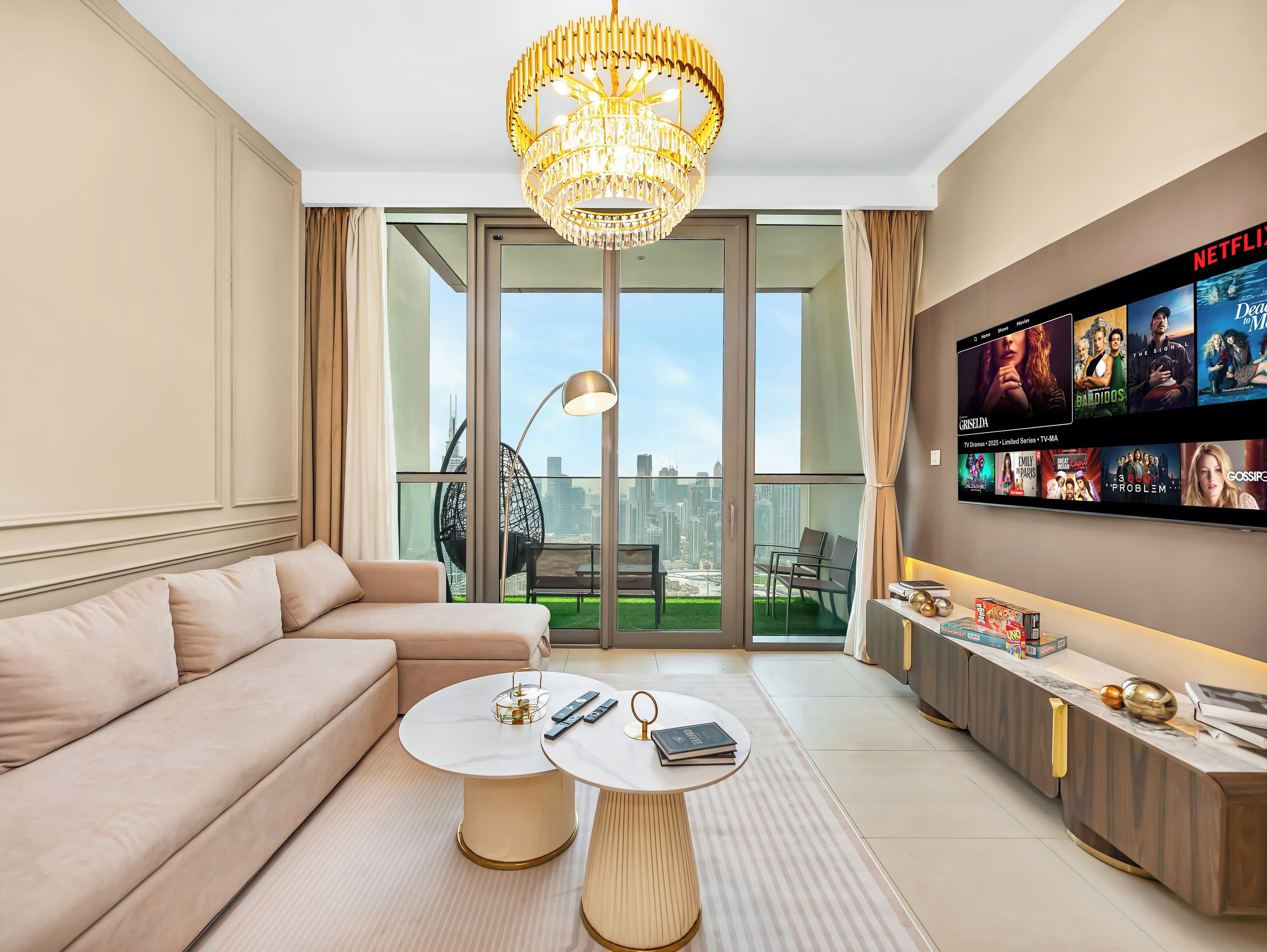 A modern living room with a sofa, two round tables, a chandelier, and a TV wall displaying various shows.