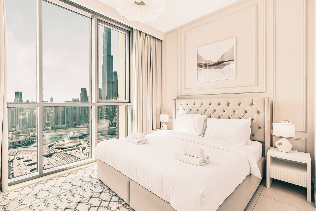 A hotel room with a large window offering a city view, a neatly made bed, and a modern design.