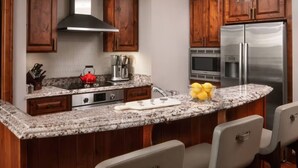 Eine Küche mit Holzausstattung, einem Edelstahlkühlschrank, Granit Arbeitsplatten und einer integrierten Kücheninsel mit Barhocker.