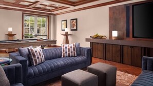 Ein Wohnzimmer mit Poolbillard, einer Couch, Poufs und einer Bar.