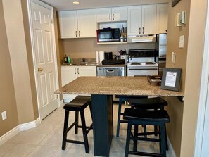 A kitchen with white cabinets, a granite countertop, and two black stools.