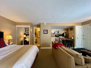 A hotel room with a bed, a sofa, a kitchenette, and a bathroom visible through an open door.