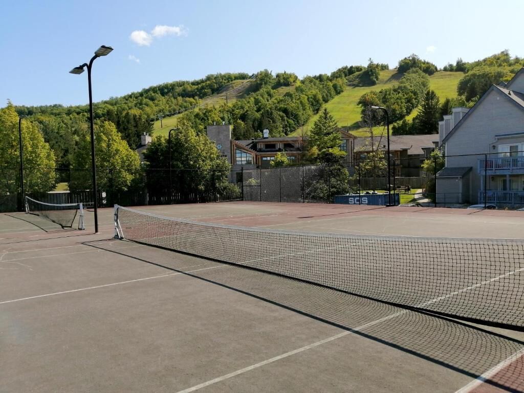 Een tennisbaan met net, omringd door een hek, en gebouwen op de achtergrond.