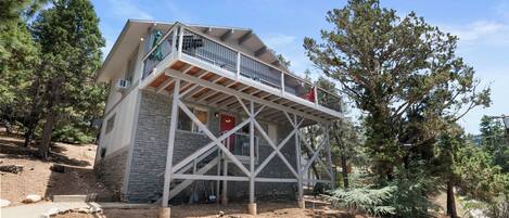 Une maison à deux étages avec un balcon, entourée d’arbres et dotée de fondations en pierre.
