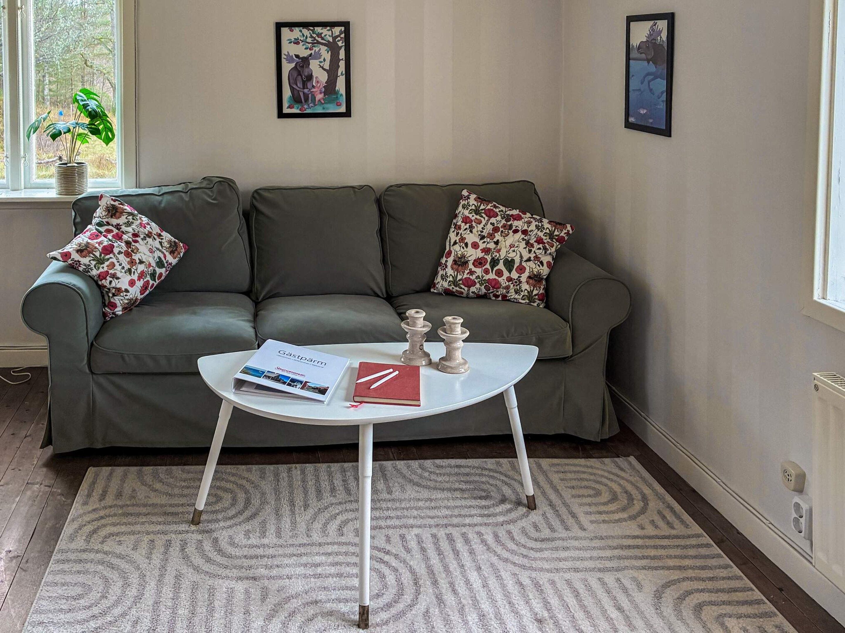 A room with a grey sofa, two floral pillows, a white coffee table with a magazine and a book, and two framed pictures on the wall.