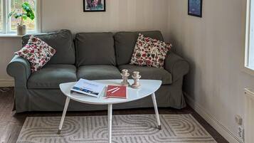A room with a grey sofa, two floral pillows, a white coffee table with a magazine and a book, and two framed pictures on the wall.