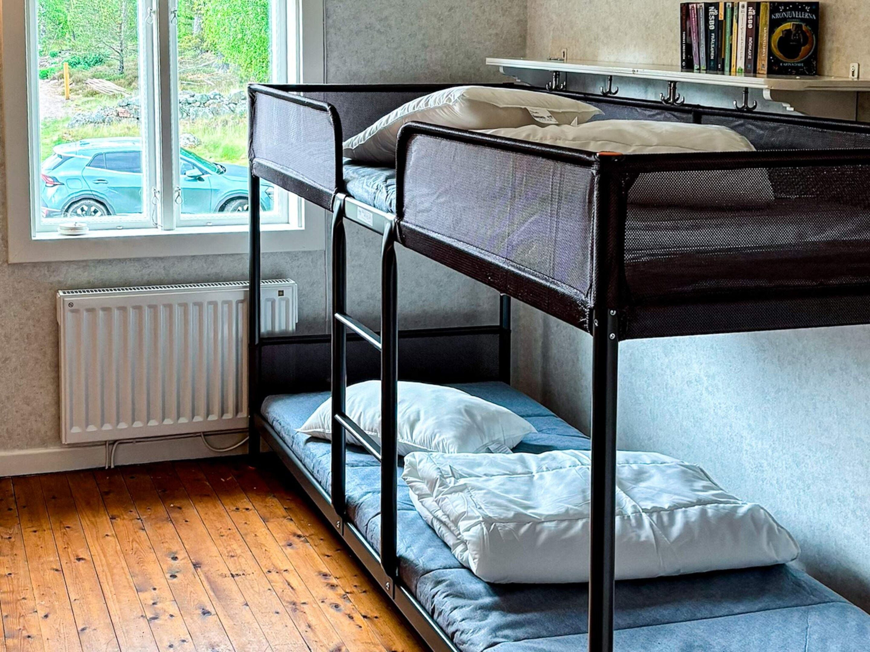 A bunk bed room with a window, radiator, and books on a shelf.