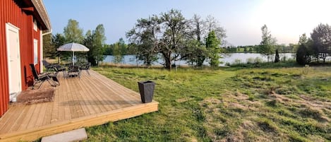A wooden deck with outdoor furniture, a trash bin, and a view of a lake.