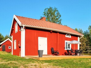 Een rode schuur in Amerikaanse bouwstijl met een witte deur, een klein terras met stoelen en een tafel.