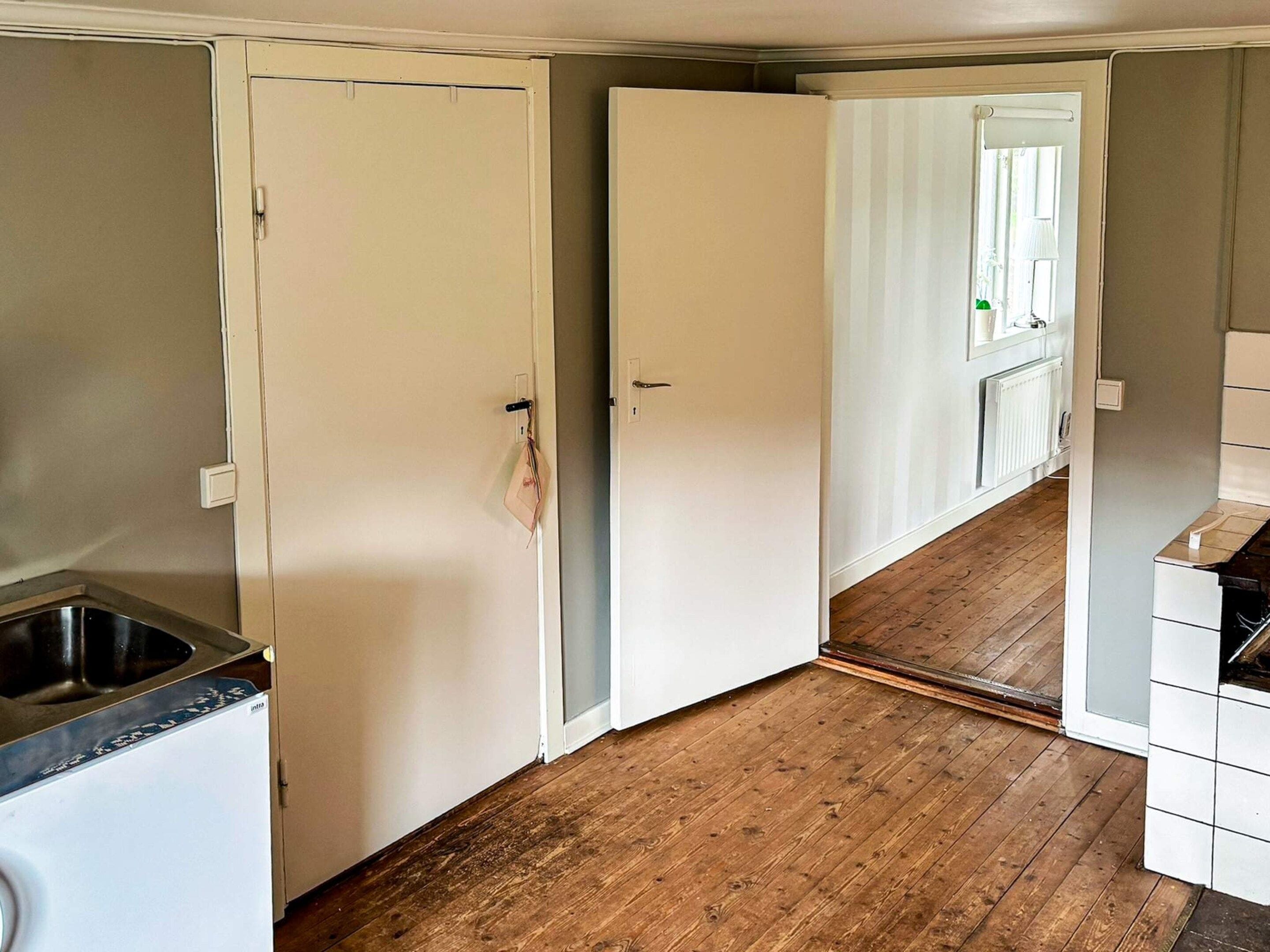 A kitchen with a wooden floor, a white refrigerator, and a white door.