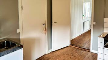 A kitchen with a wooden floor, a white refrigerator, and a white door.