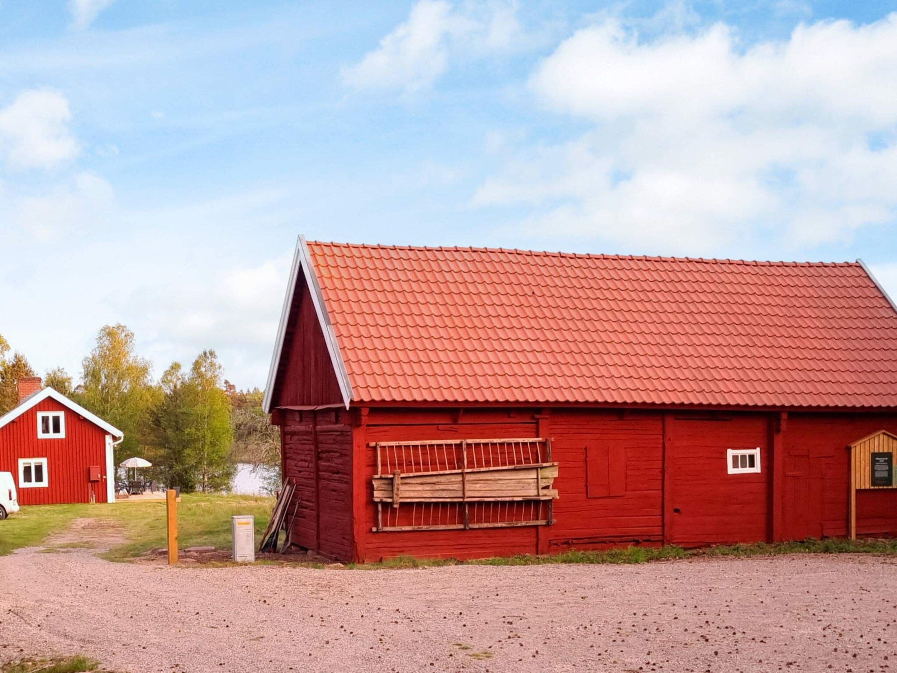 A red barn with a sloped roof, a gravel driveway, and a small wooden structure to the left.