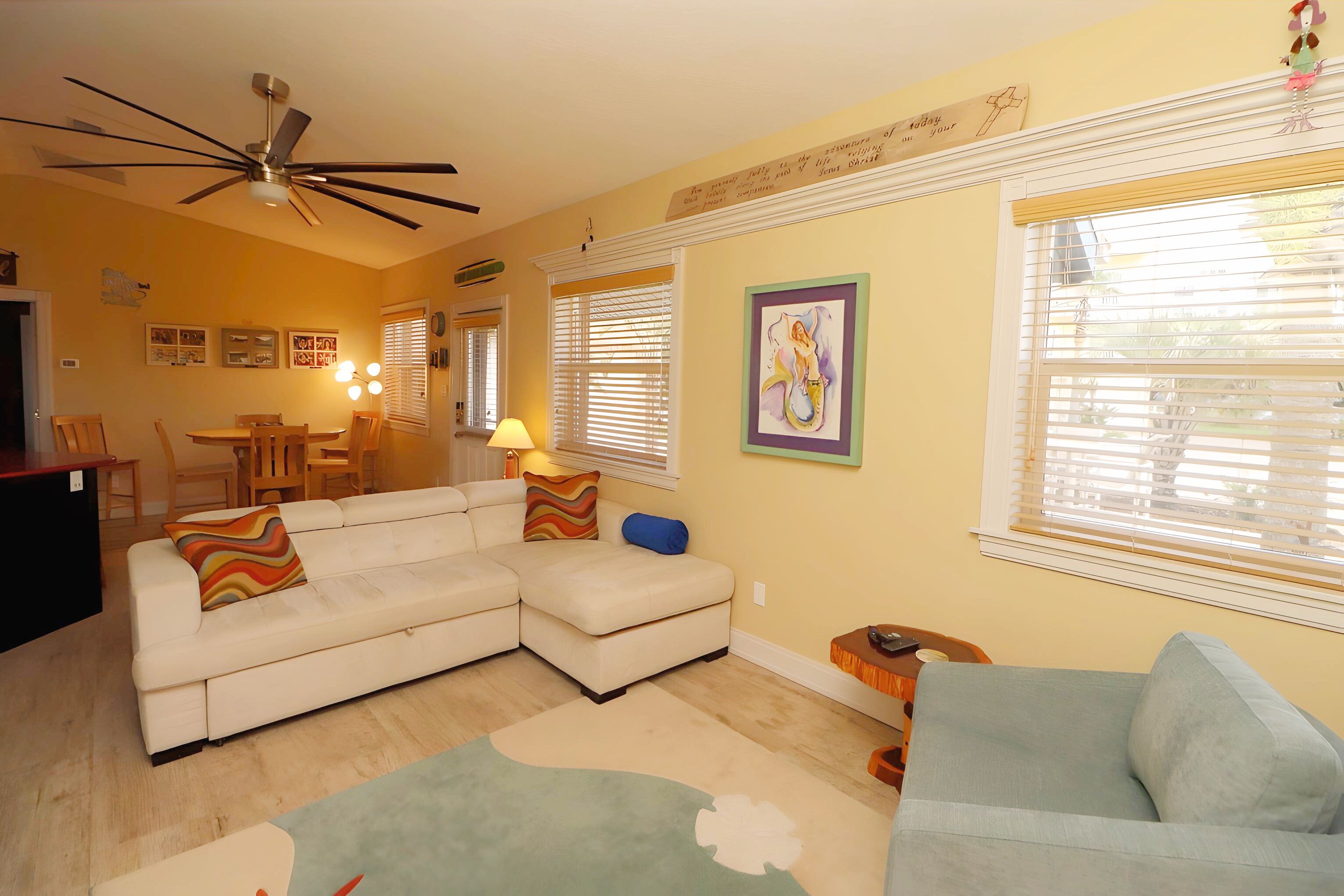 A living room with a sectional sofa, a blue armchair, a dining table, and a ceiling fan.