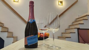 A bottle of Hungary Rosé Extra Dry wine and two empty wine glasses on a table with a staircase in the background.