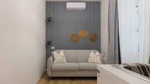 A modern living room with a grey sofa, a white air conditioner, and three woven wall decorations. - Stylish Gem in Historic Trieste  (Trieste)