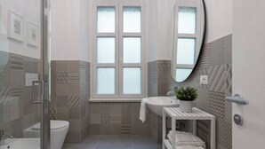 A modern bathroom with a glass shower enclosure, a toilet, a sink, and a mirror. - Stylish Gem in Historic Trieste  (Trieste)