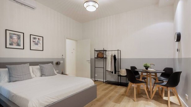 A modern bedroom with a large bed, a bedside table, a wardrobe, and a dining area with chairs and a table. - Stylish Gem in Historic Trieste  (Trieste)