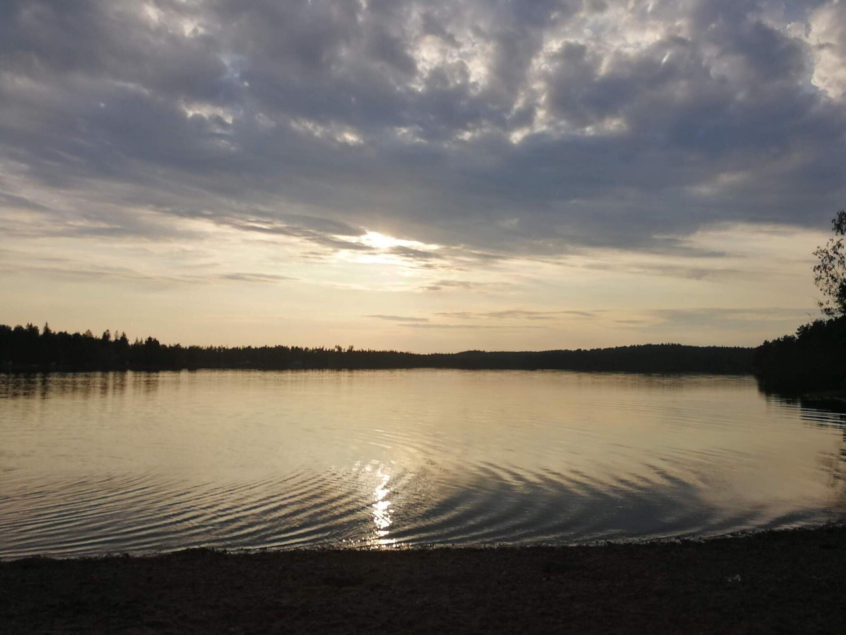 A calm lake with a forested shoreline and a cloudy sky.