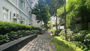 Un chemin bordé de verdure et un bâtiment doté de nombreuses fenêtres et de plusieurs unités de climatisation.