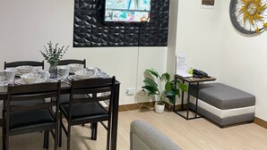 Un salon moderne comprenant un coin repas, un téléviseur fixé au mur, un élément décoratif mural et une petite table agrémentée d’une plante.