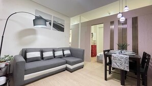 Un salon moderne avec un canapé gris, une table à manger dressée avec des assiettes et un vase, et un grand lampadaire.
