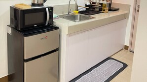 Une cuisine compacte équipée d’un four à micro-ondes, d’une bouilloire et d’un réfrigérateur en acier inoxydable. Des étagères au-dessus du plan de travail servent à ranger la vaisselle, et une hotte aspirante est installée au-dessus de la cuisinière.