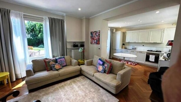 A living room with a beige sofa, a coffee table, and a rug. There is a kitchen in the background with white cabinets and a sink. - Historic house with garden across from NYU Florence (Unknown)