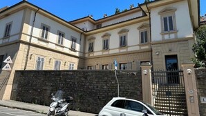A two-story building with a stone wall and a gated entrance. - Historic house with garden across from NYU Florence (Unknown)