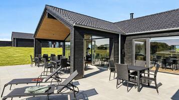 Un espace extérieur aménagé en terrasse, avec des tables et des chaises, un coin salon abrité et une vue sur le paysage environnant.