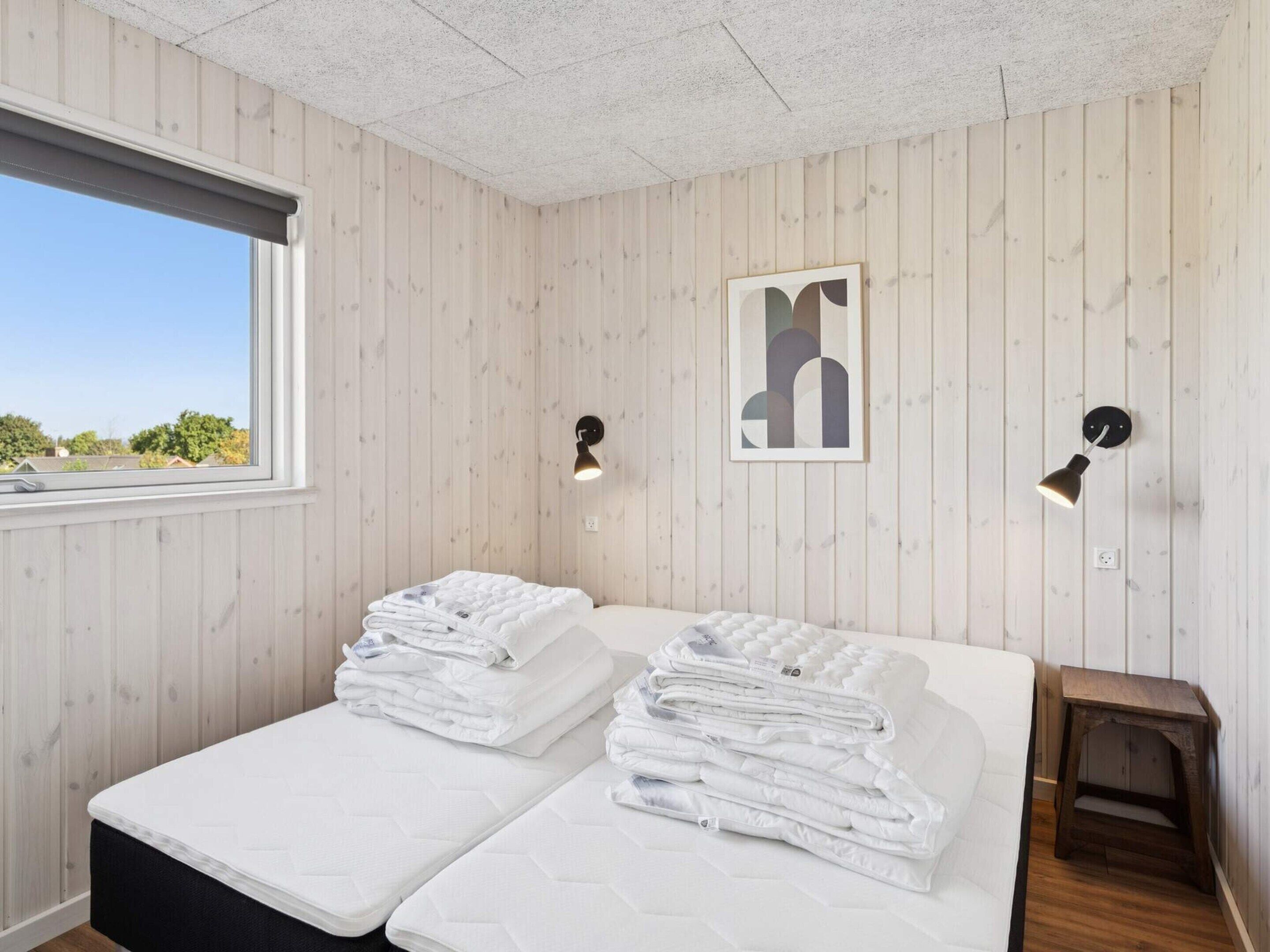 A room with two beds, a window, and a wall-mounted light fixture.