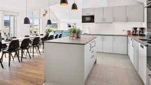 A modern kitchen with white cabinets, a central island, and pendant lighting. - 5 Star Holiday Home in Bogense (Bogense)
