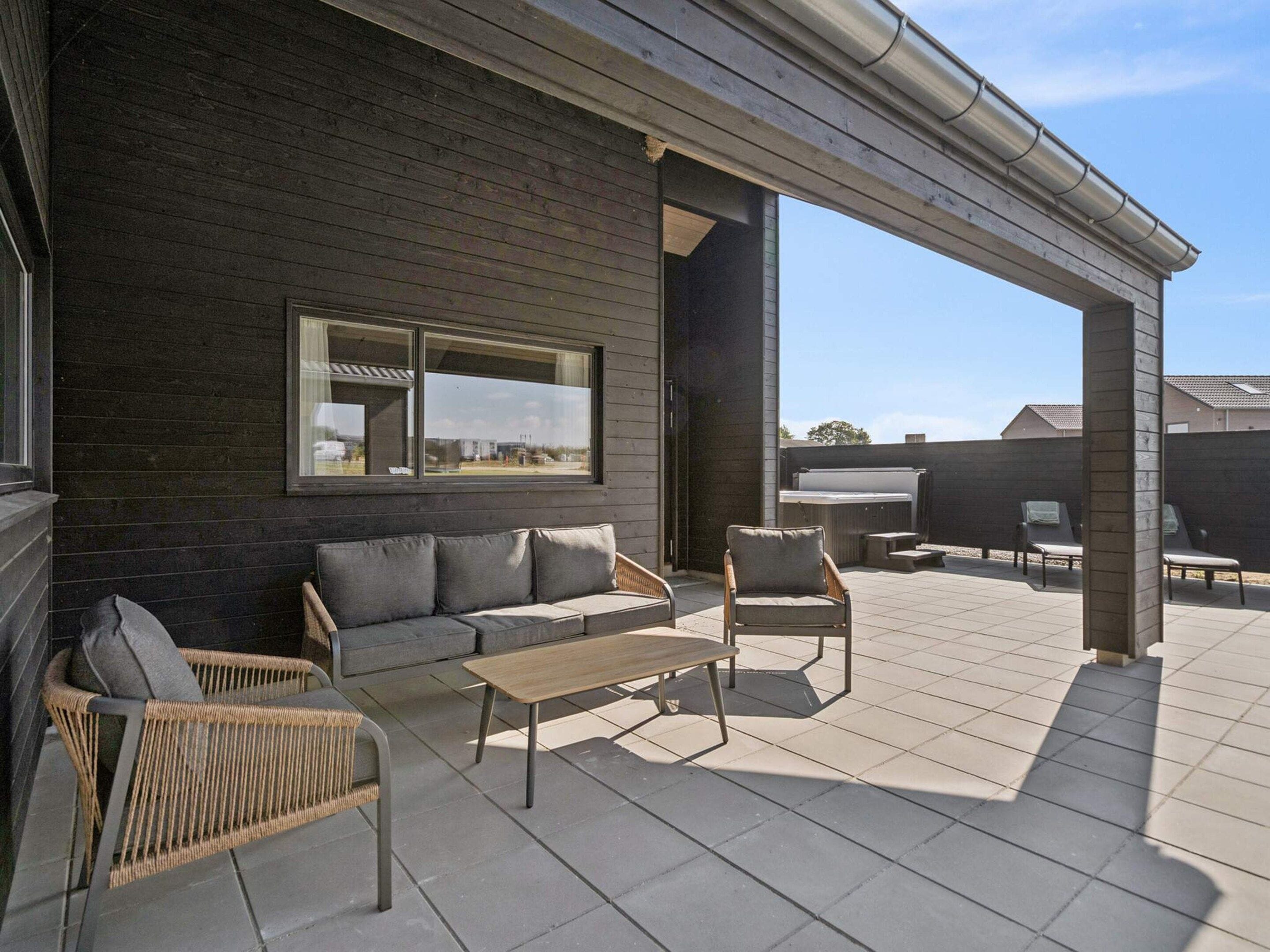 Une terrasse extérieure couverte, aménagée avec un canapé, des fauteuils et une table.