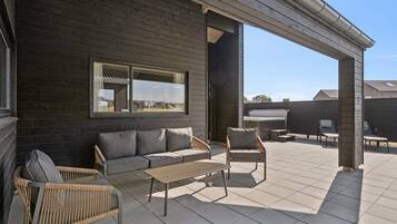 Une terrasse extérieure couverte, aménagée avec un canapé, des fauteuils et une table.