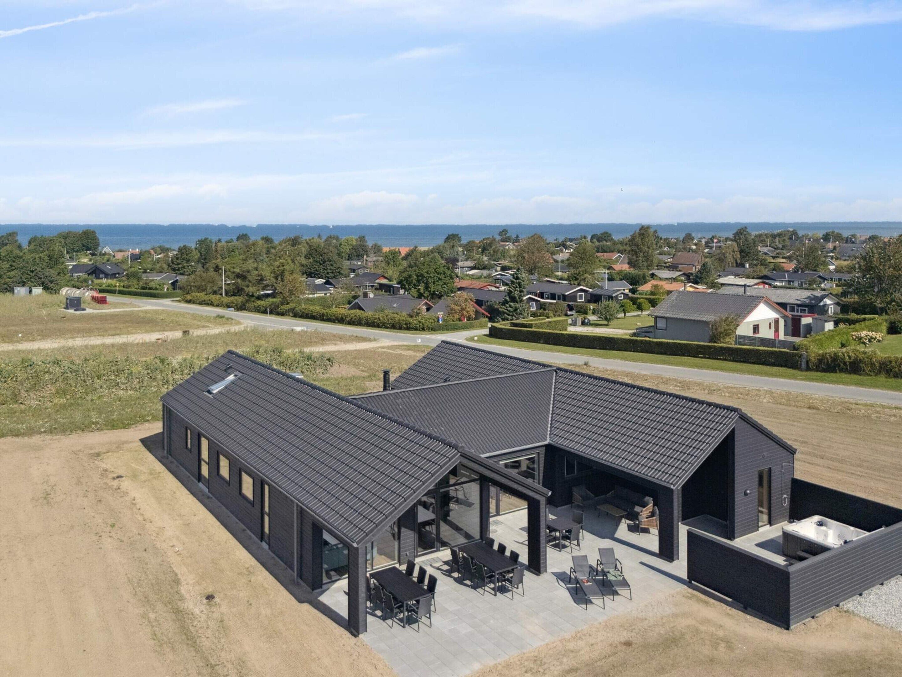 Ett modernt hus med en stor uteplats, en täckt sittgrupp utomhus och utsikt över det omgivande bostadsområdet.