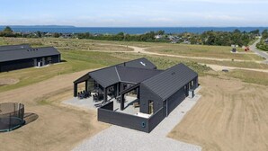 A modern building with a large patio area, surrounded by open fields and a view of the sea. - 5 Star Holiday Home in Bogense (Bogense)