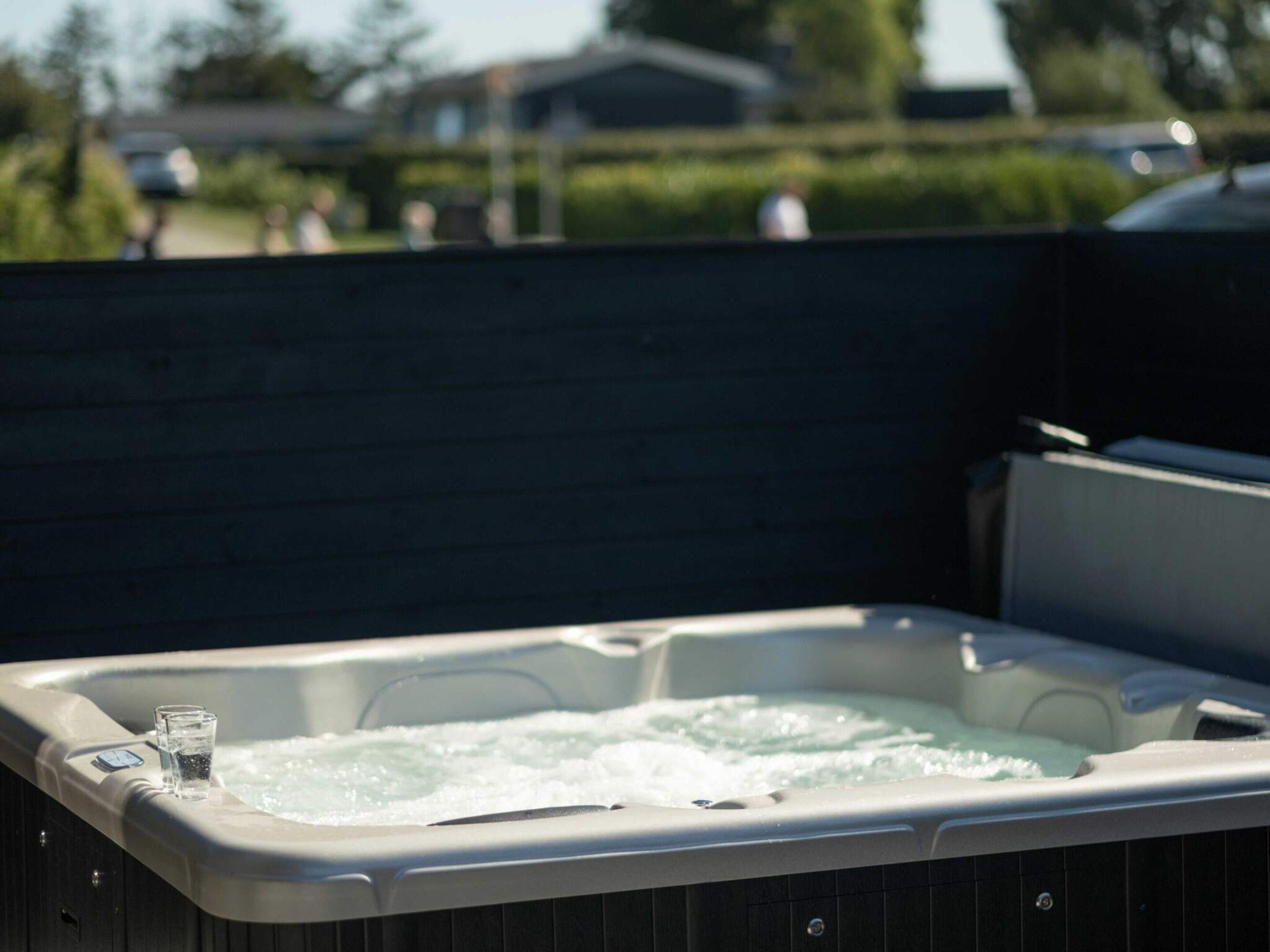 A hot tub with a glass of water on the edge, surrounded by a dark fence.