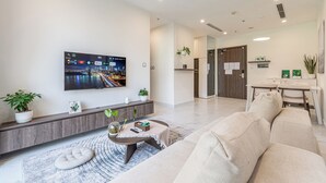 A modern living room with a flat-screen TV, a sofa, a coffee table, and a dining area with a table and chairs.