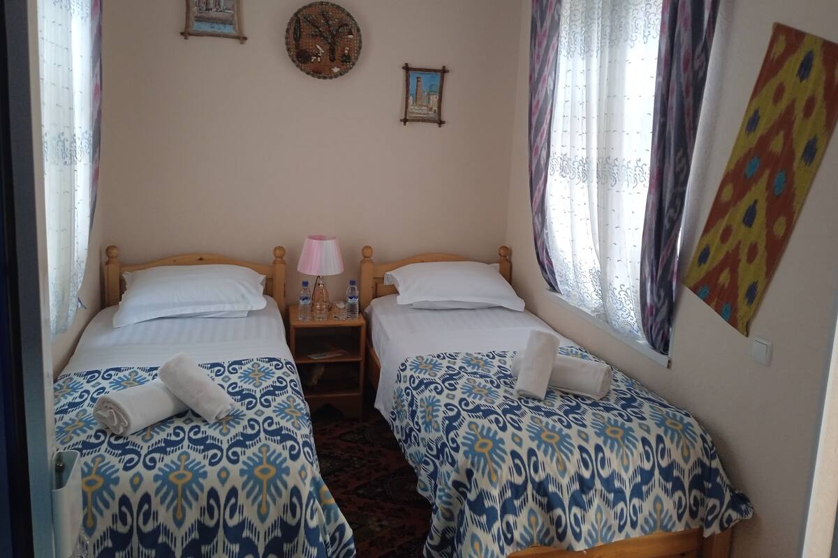 A bedroom with two beds, a nightstand with a lamp, and a window with curtains.