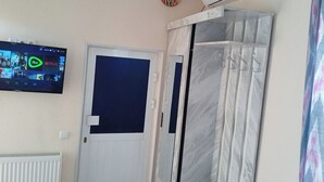 A room with a television mounted on the wall displaying a program, a white door with a blue panel, and a white radiator. - Guest House An & Tea House (Bukhara)
