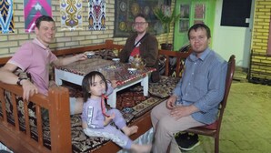 A family sitting at a table with patterned tablecloths, surrounded by decorative wall hangings and a green door. - Guest House An & Tea House (Bukhara)