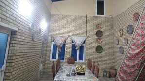 A dining area with a brick wall, a table with chairs, and decorative plates on the wall. - Guest House An & Tea House (Bukhara)
