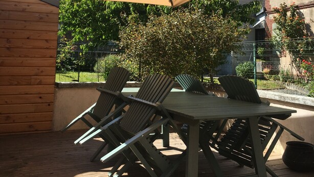 An outdoor patio with a table and chairs, a large beige umbrella, and a brick wall.