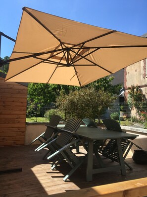 An outdoor patio with a table and chairs, a large beige umbrella, and a brick wall.